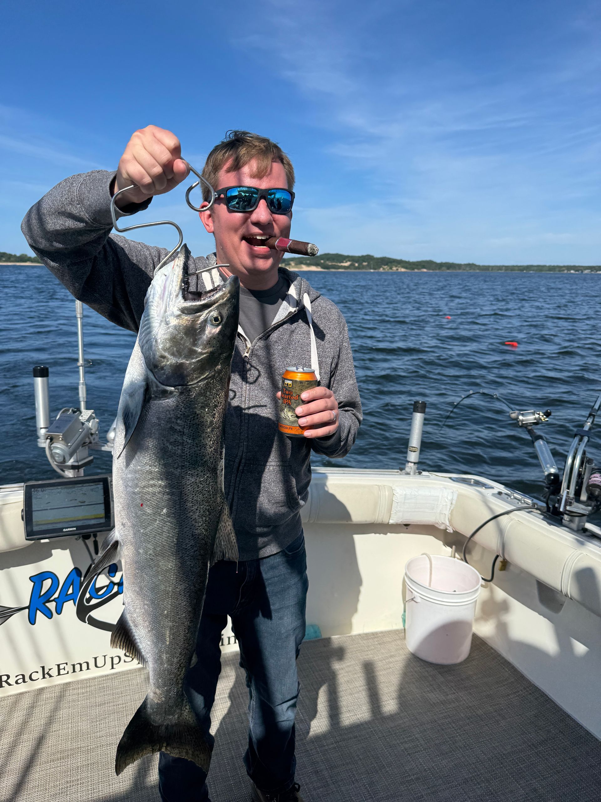 Man on boat holding large fish and drink, smiling in sunny setting.