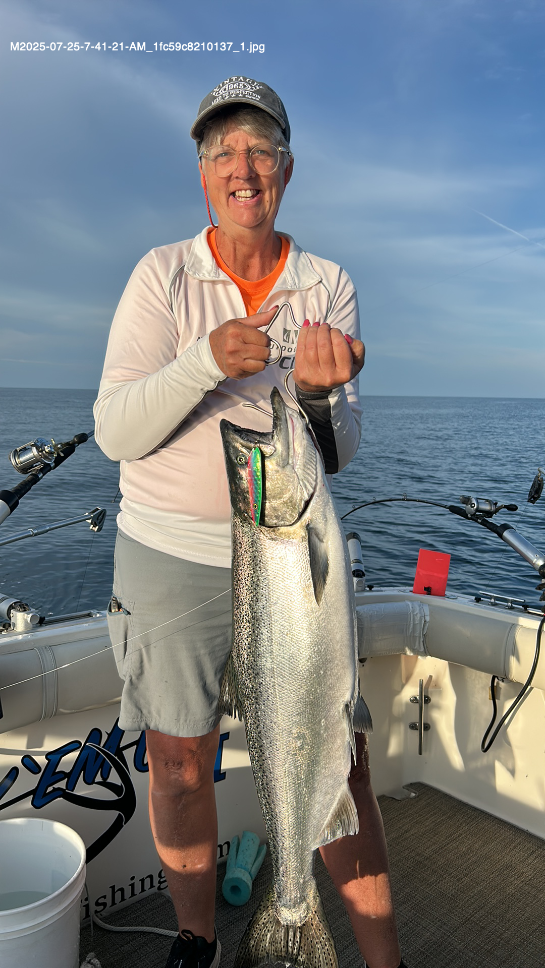 Person on boat holding a large fish, smiling. Ocean and fishing gear visible.
