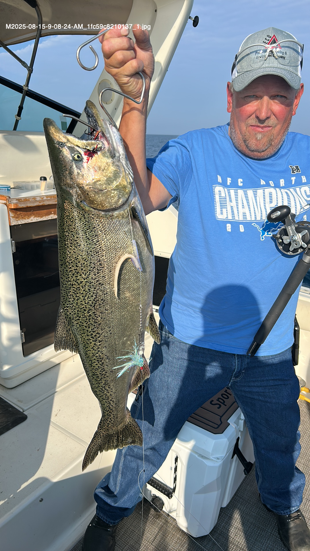 Man on boat holds up a large fish, blue water in background.