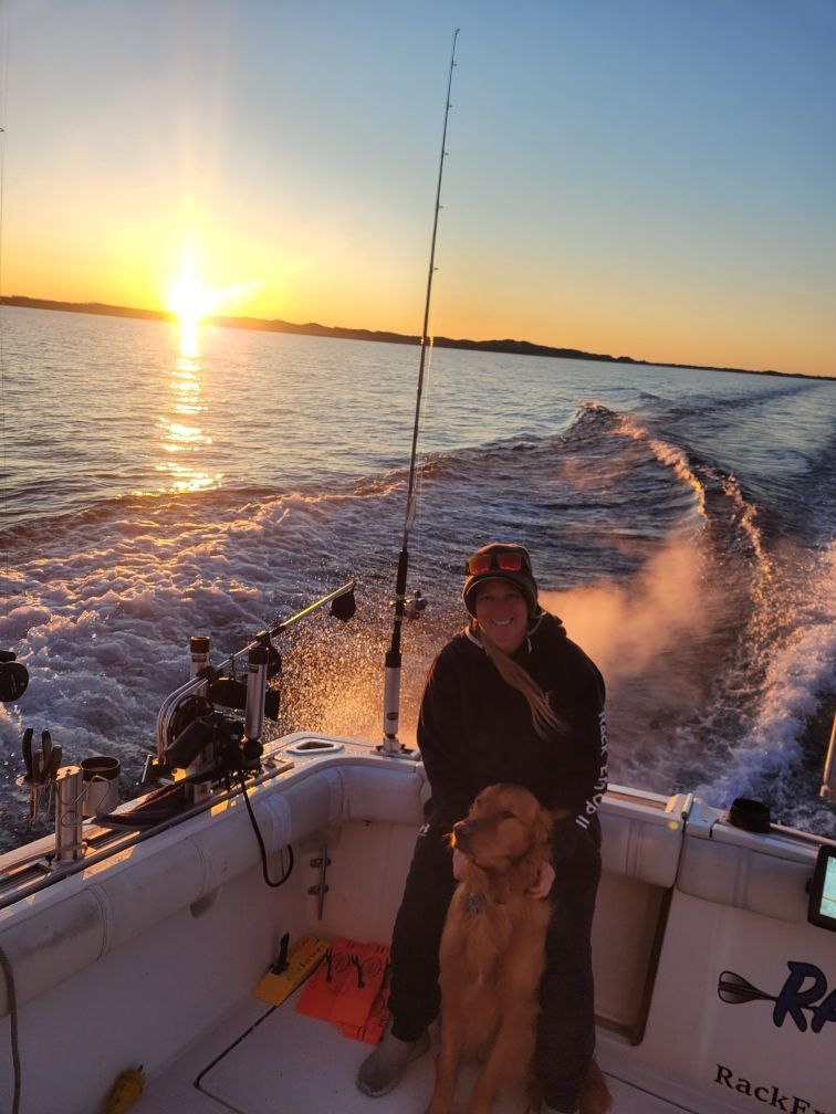 Woman and golden retriever on a boat, fishing at sunset, ocean waves visible.