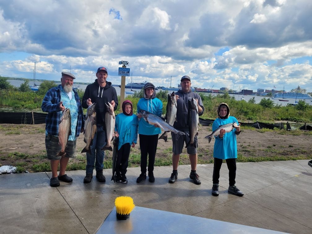 A group of people holding up fish they caught. Outdoors, cloudy sky.