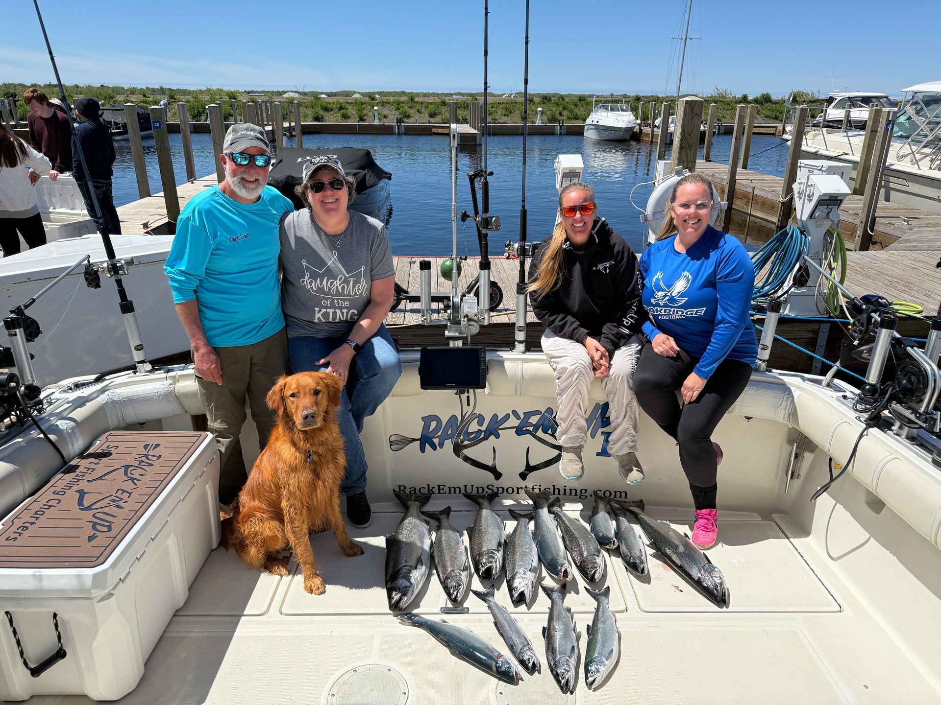 Group fishing trip on a boat with catch of fish. People smiling with a dog on a sunny day.