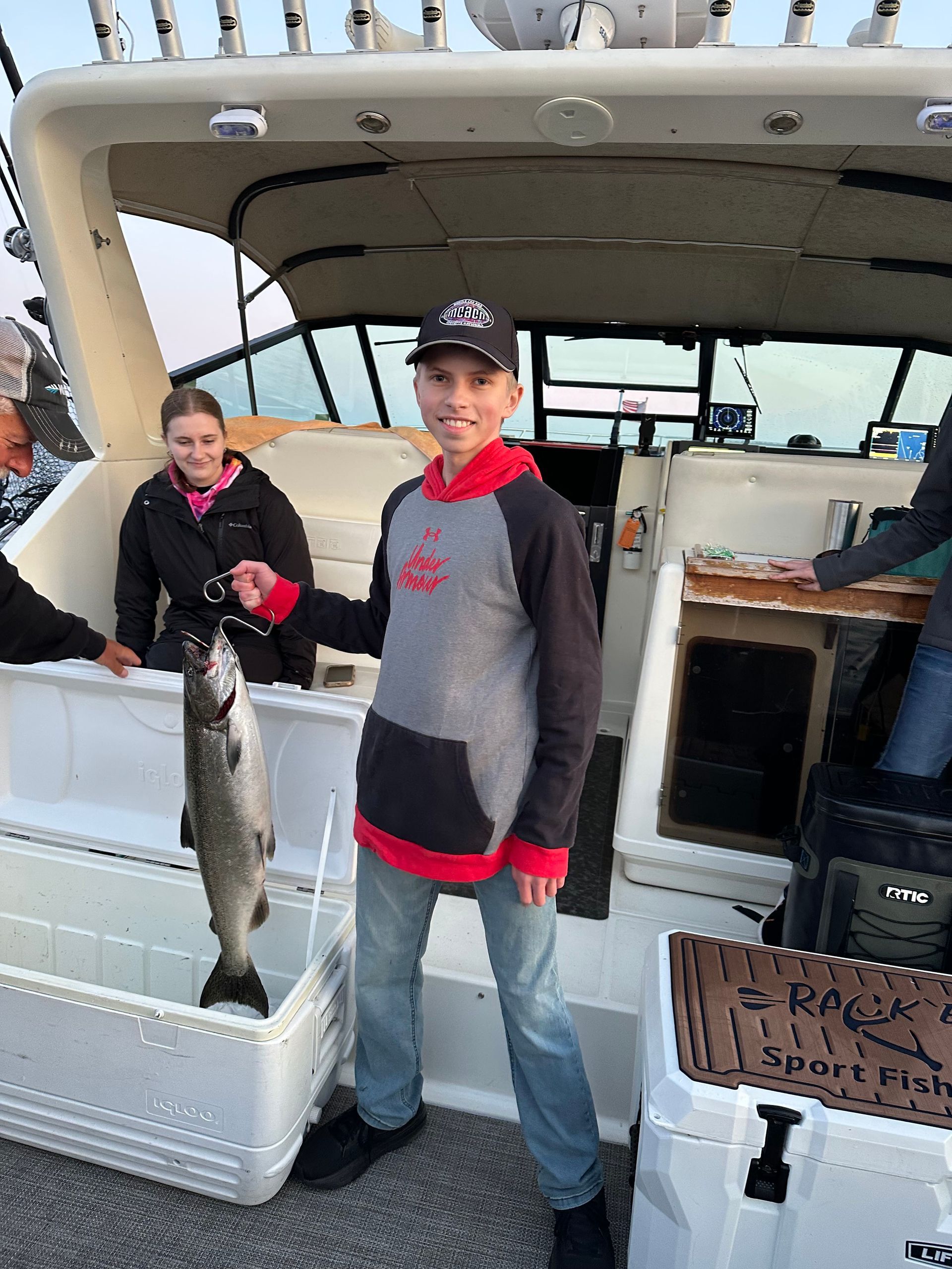 Boy holding a fish on a boat; another person nearby. They are on a sport fishing boat.