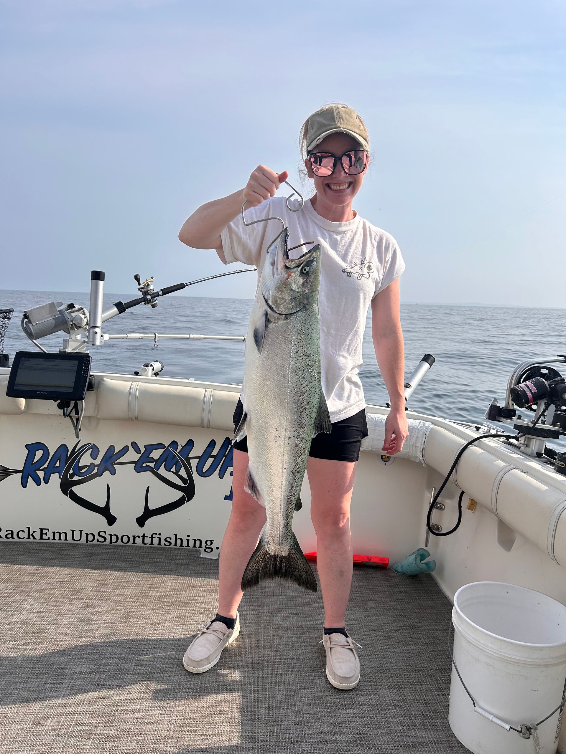 Woman on boat holds up a large fish she caught. Sunny sky, ocean in background.