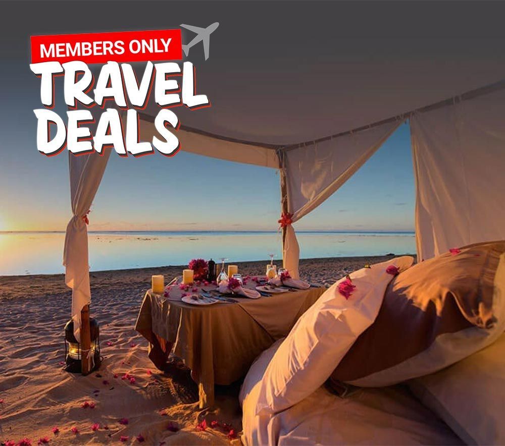 A bed under a canopy on a beach with a table and chairs.