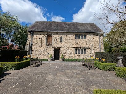 Stone building with a dark doorway, benches, and stone patio under a cloudy sky.