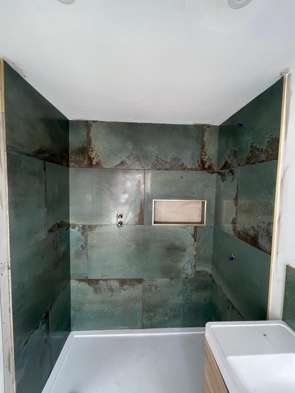 A walk-in shower with large, dark green, rustic-textured wall tiles and a rectangular recessed niche.