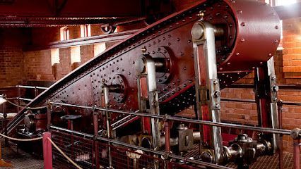 A large, red Victorian steam engine in a brick building with exposed piping.