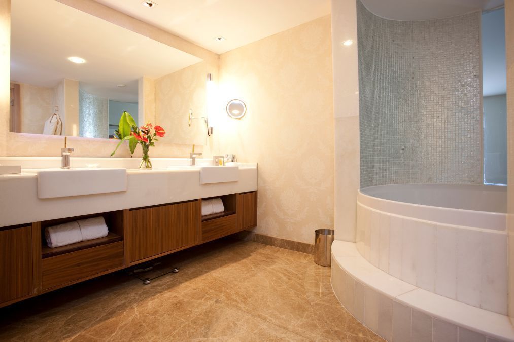 Luxurious bathroom with marble floor, double sinks, wood cabinetry, and a rounded shower.