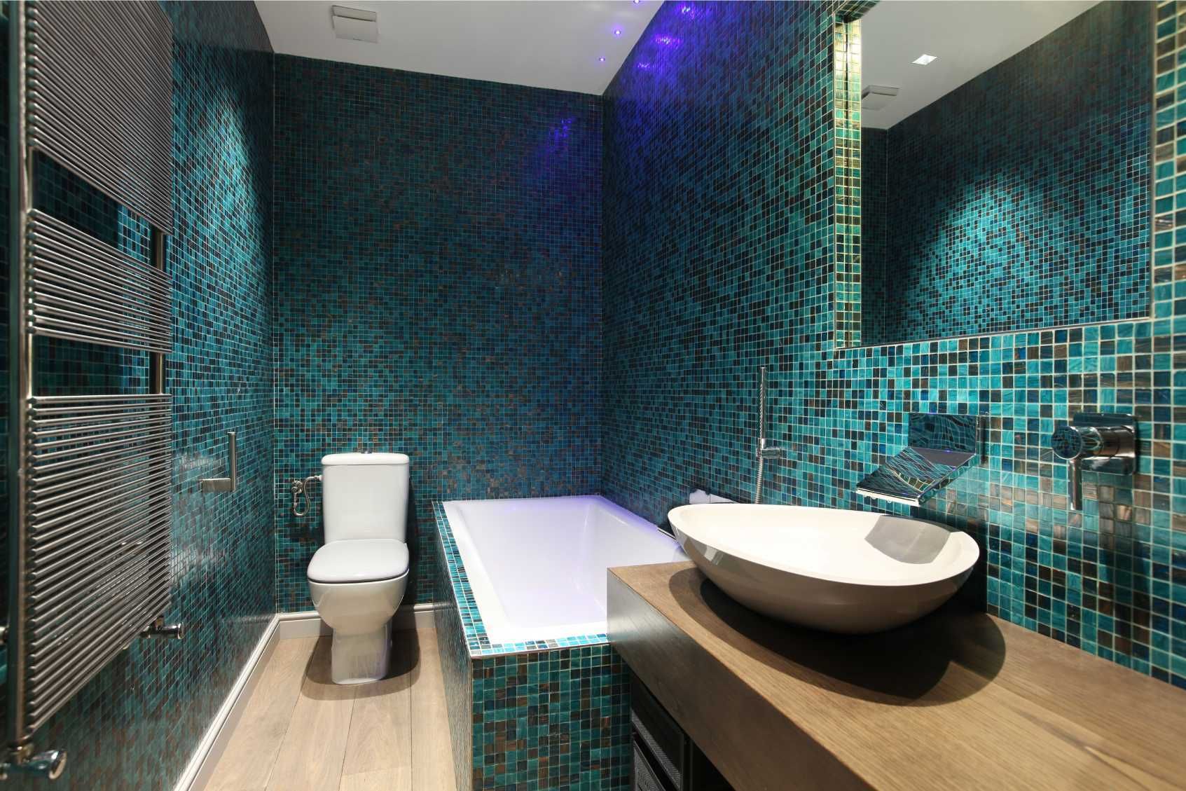Bathroom with teal mosaic tile walls, white toilet, tub, and sink, and a wooden vanity.