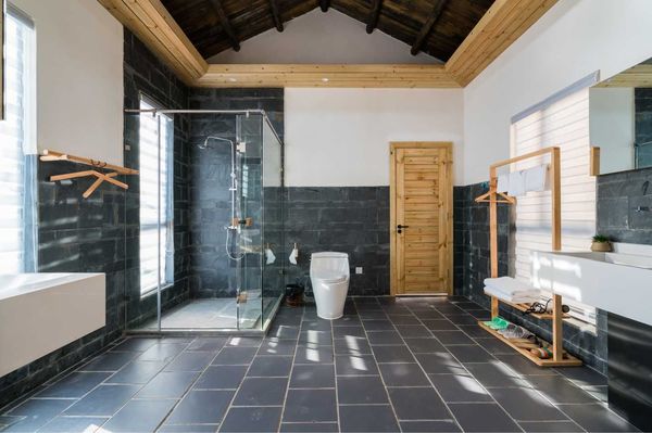 Spacious bathroom with dark gray tile, glass shower, wooden door and accents, and bright natural light.