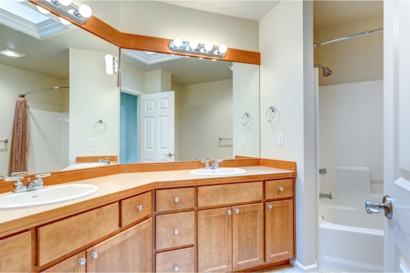 Bathroom with double sinks, light wood cabinets, large mirror, and a shower/tub combo.