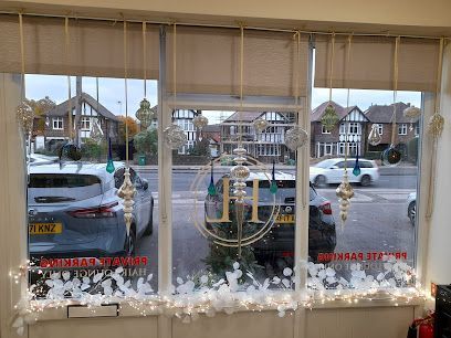 A shop window decorated with holiday ornaments, overlooking a street with parked cars and houses.