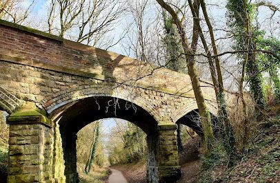 Brick and stone arched bridge over a path through a wooded area.