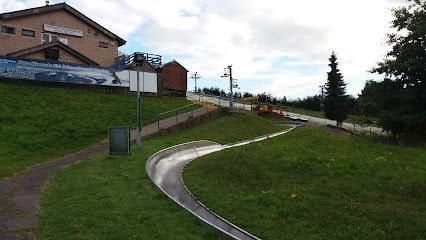 Curving metal track on grassy hill, near a building. Outdoor recreation area on a cloudy day.