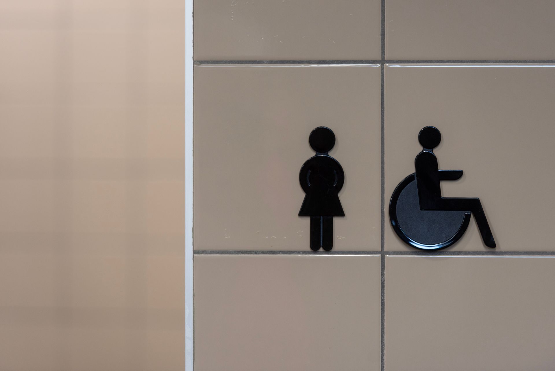 Restroom signs for women and wheelchair accessibility on beige tiled wall
