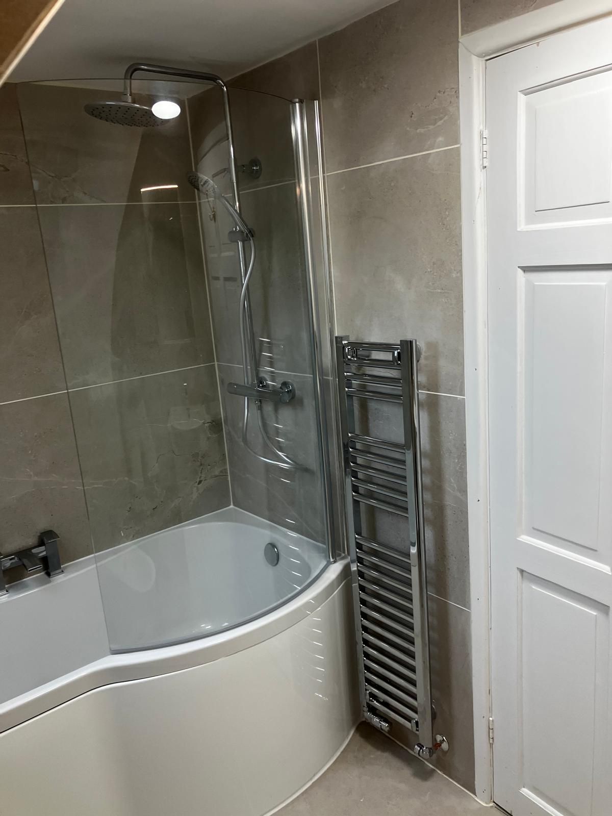 Bathroom with a curved-edge bathtub, showerhead, glass screen, towel rack, and white door. Beige wall tiles.