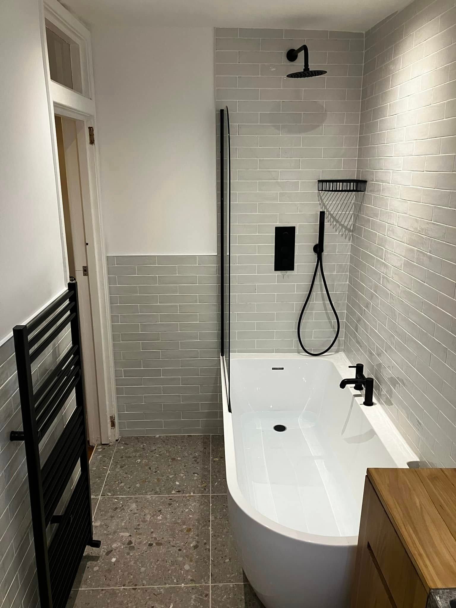 Modern bathroom with white tub, black fixtures, gray tiled walls, and black towel rack.