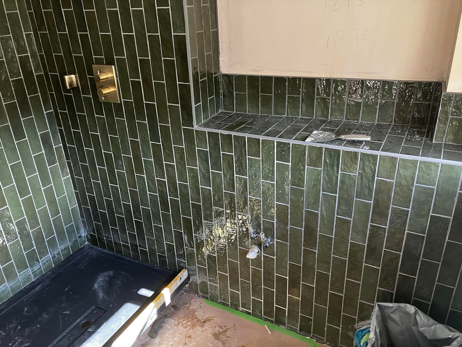 Green tiled shower with gold fixtures and pink wall, under construction.
