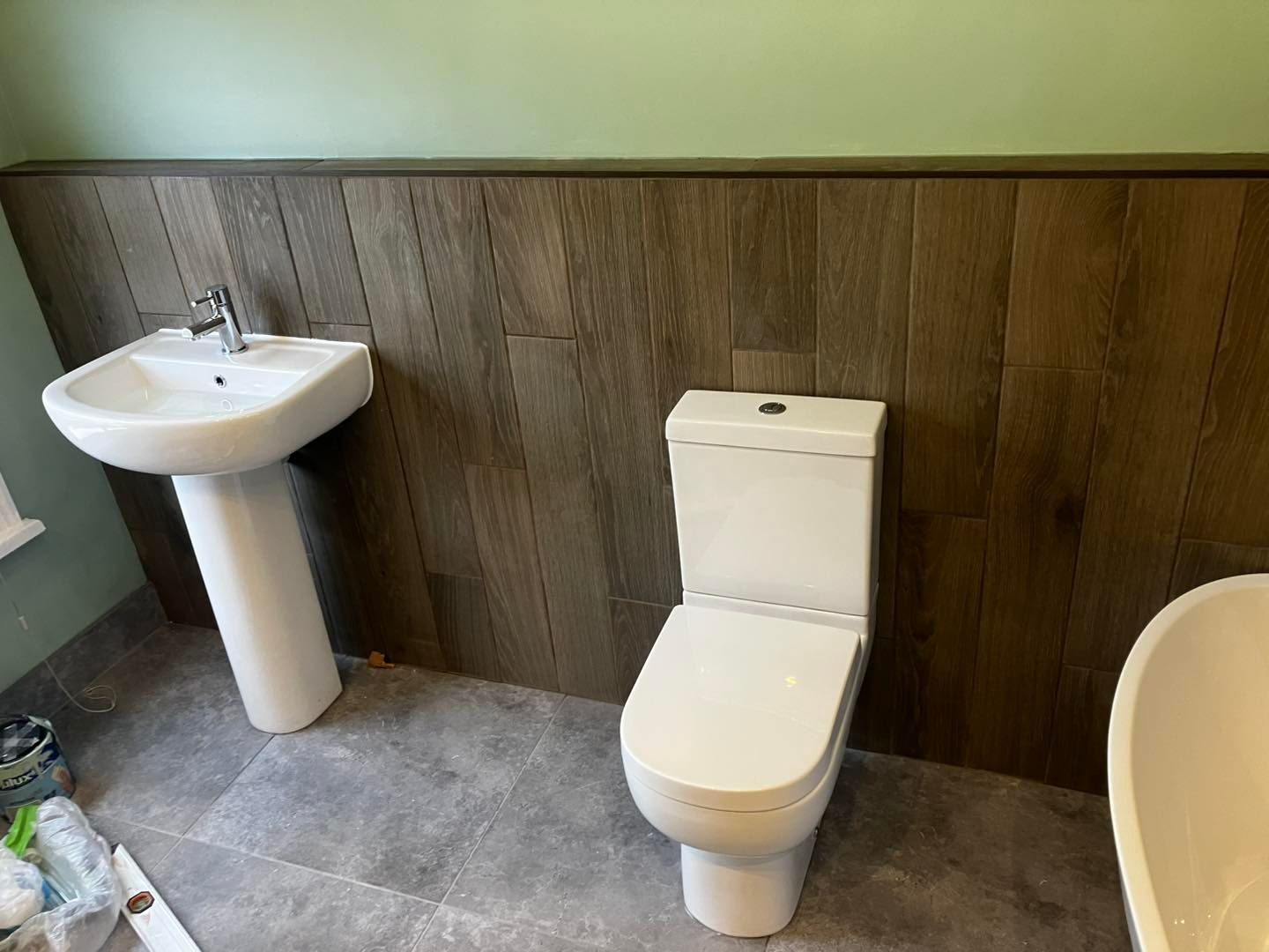 Bathroom with a white pedestal sink, toilet, and wood paneling on the wall; gray floor.