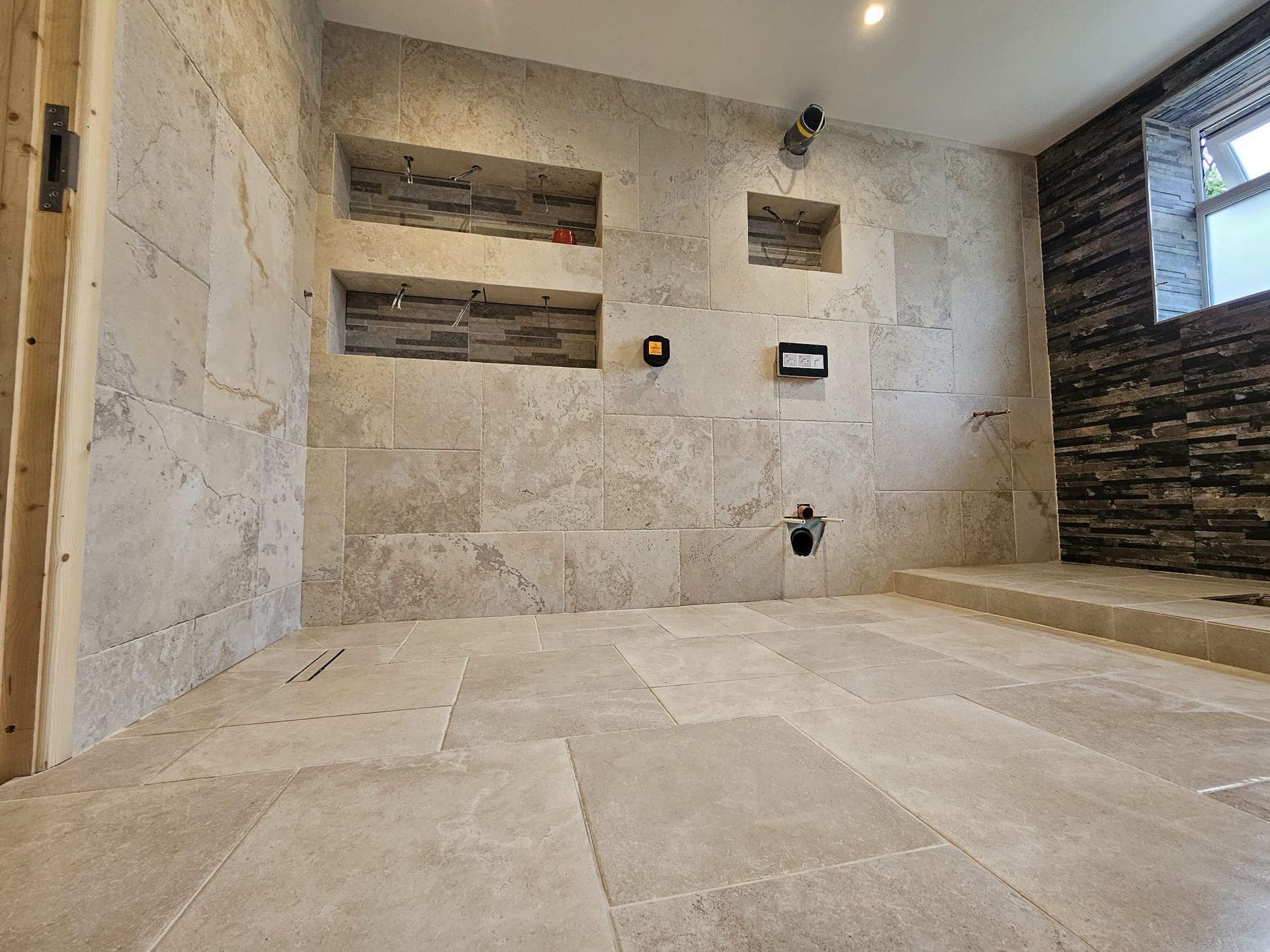 A bathroom interior with light-colored stone walls and floor, featuring recessed shelves and plumbing fixtures.