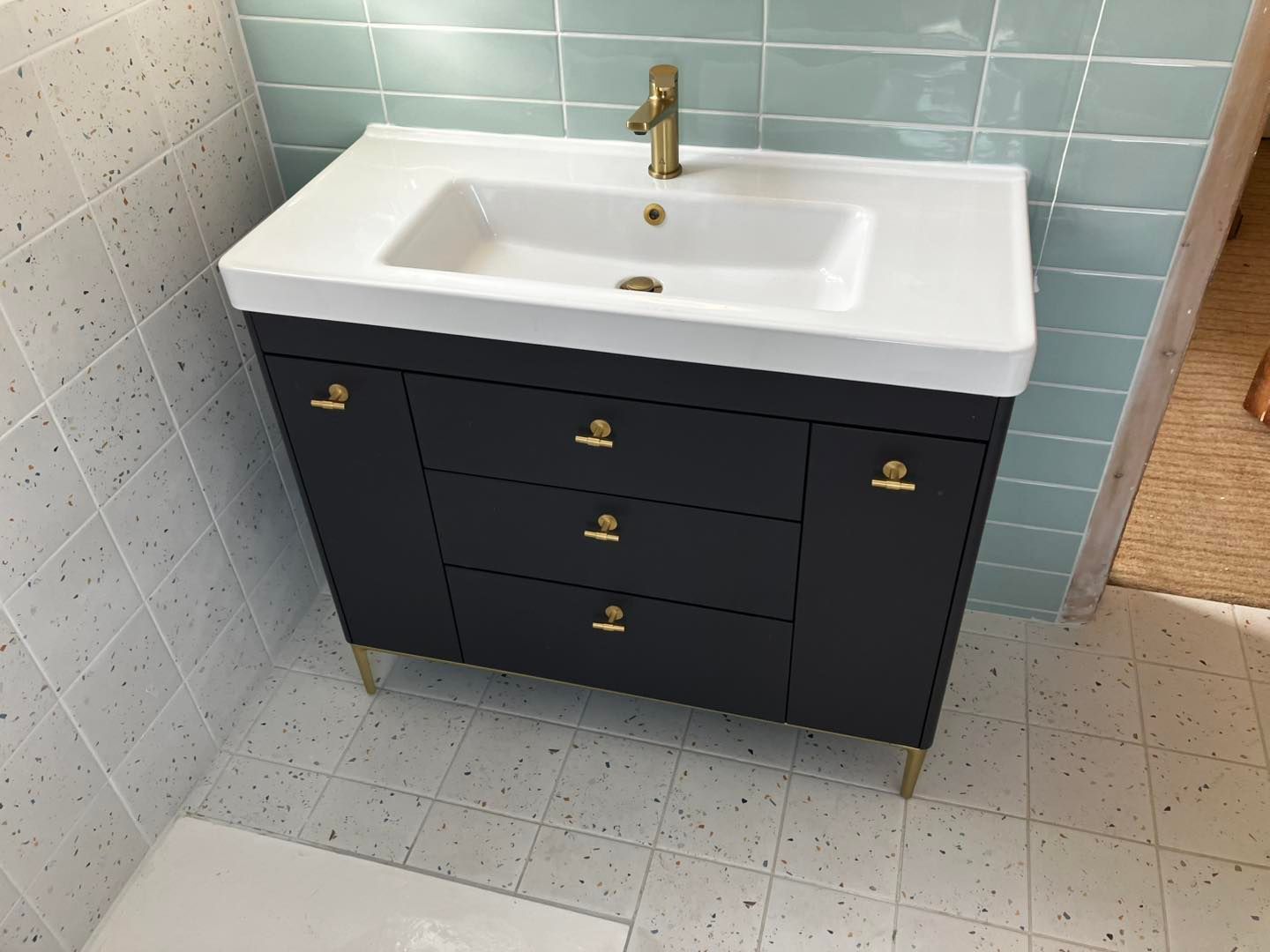 Bathroom vanity with dark gray cabinet, white sink, gold fixtures, and tile backsplash.