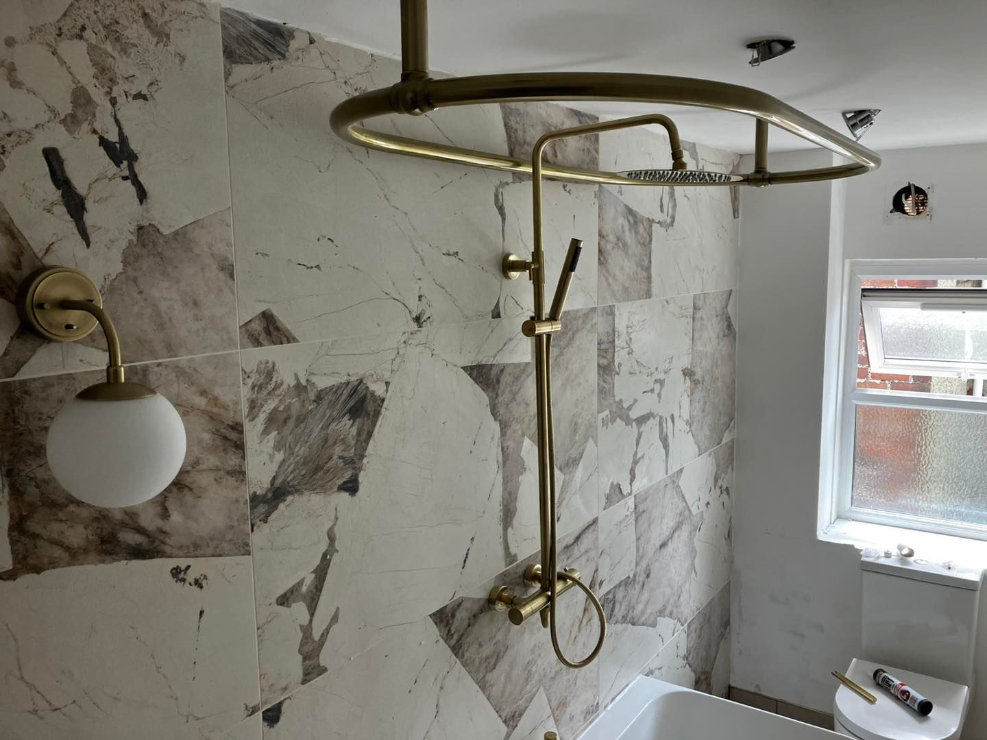 A bathroom with a marble-tiled shower, brass fixtures, and a globe-shaped wall light.