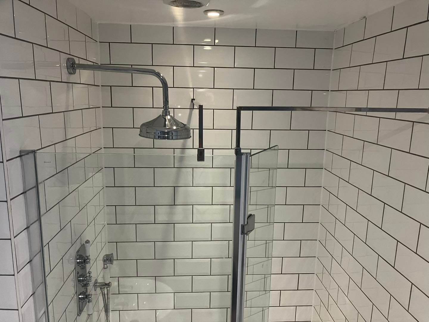 White-tiled shower with glass doors and silver showerhead.