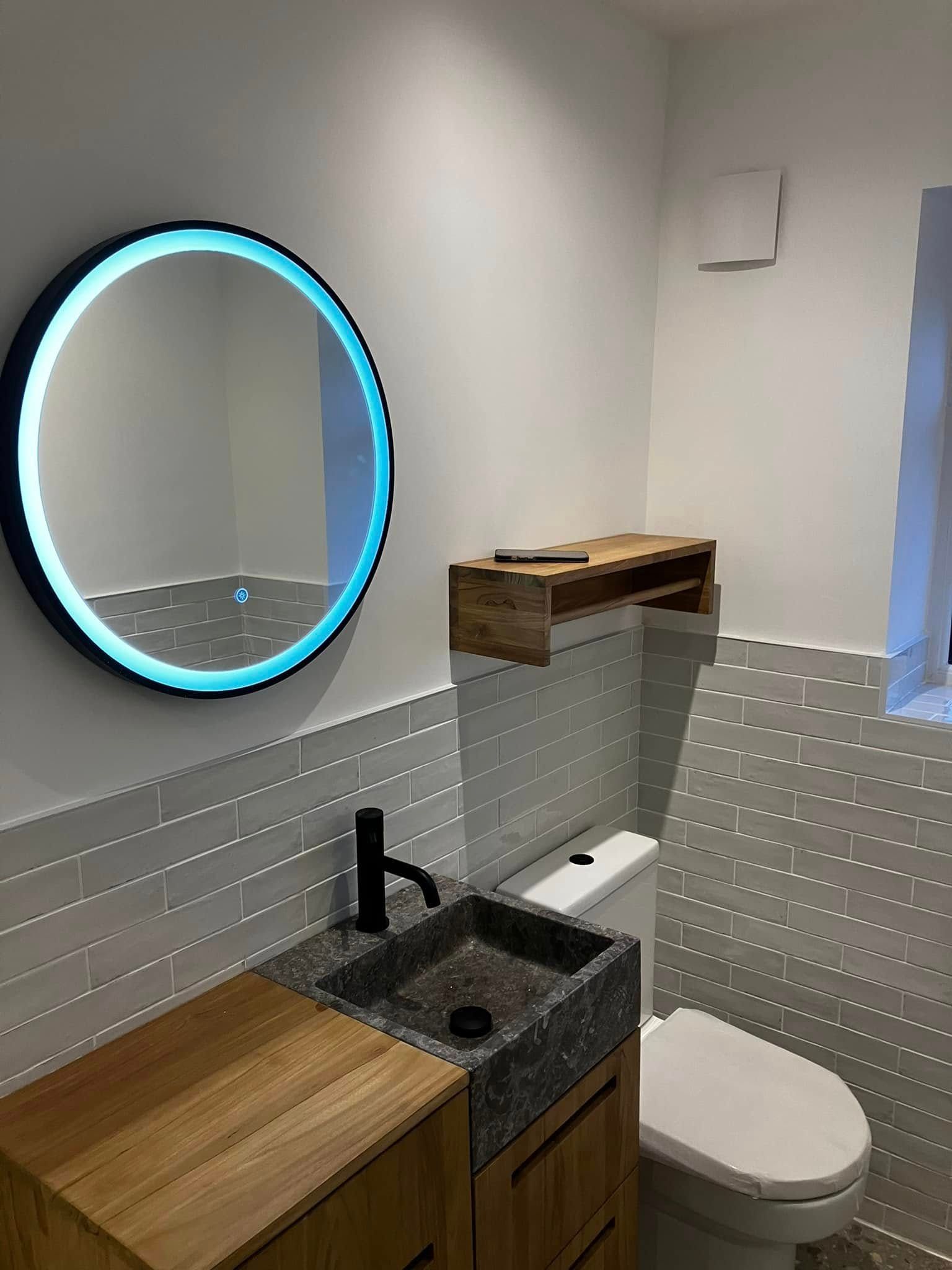 Small modern bathroom with a round mirror, wooden vanity, and toilet.