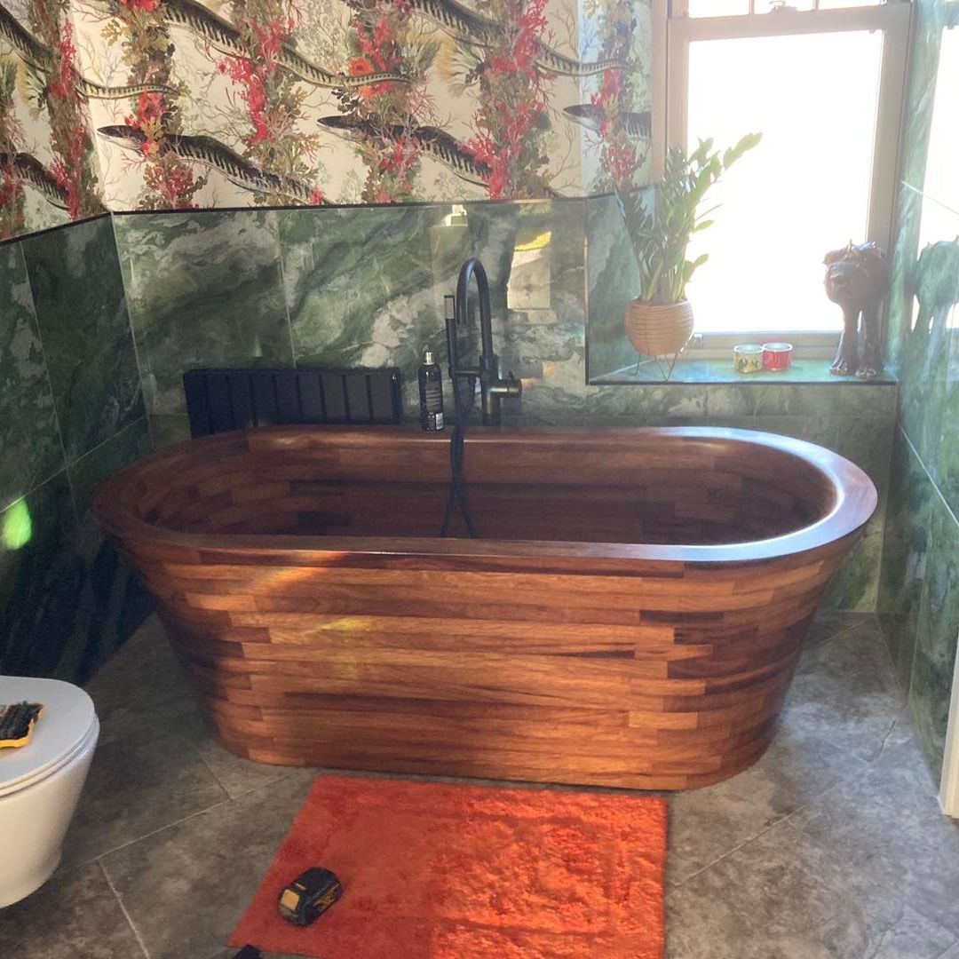 Wooden bathtub in bathroom with floral wallpaper and marble walls, orange rug.