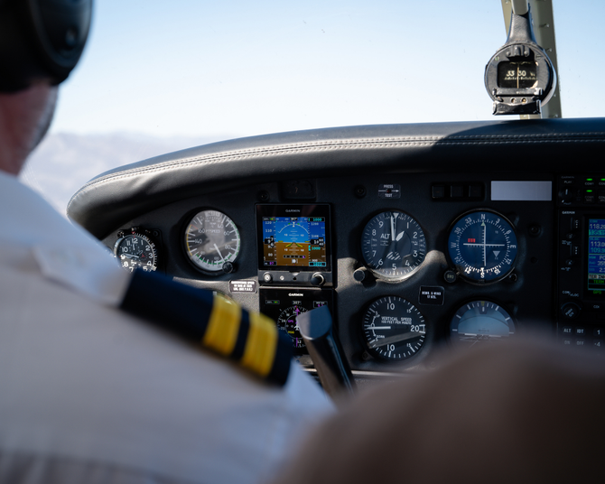 Pilot in uniform looking at an aircraft's instrument panel during flight.