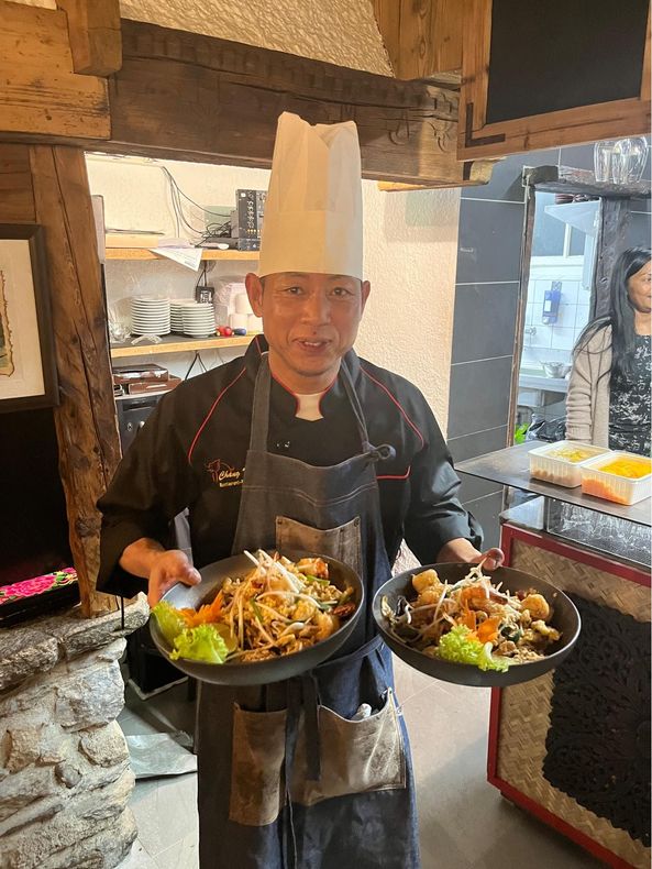 Un chef tient deux assiettes de nourriture dans une cuisine.