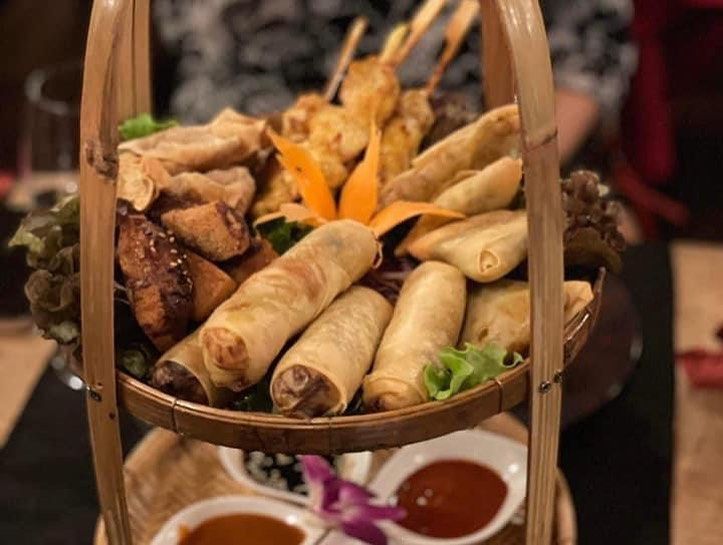 Un panier rempli de rouleaux de printemps et de brochettes sur une table.
