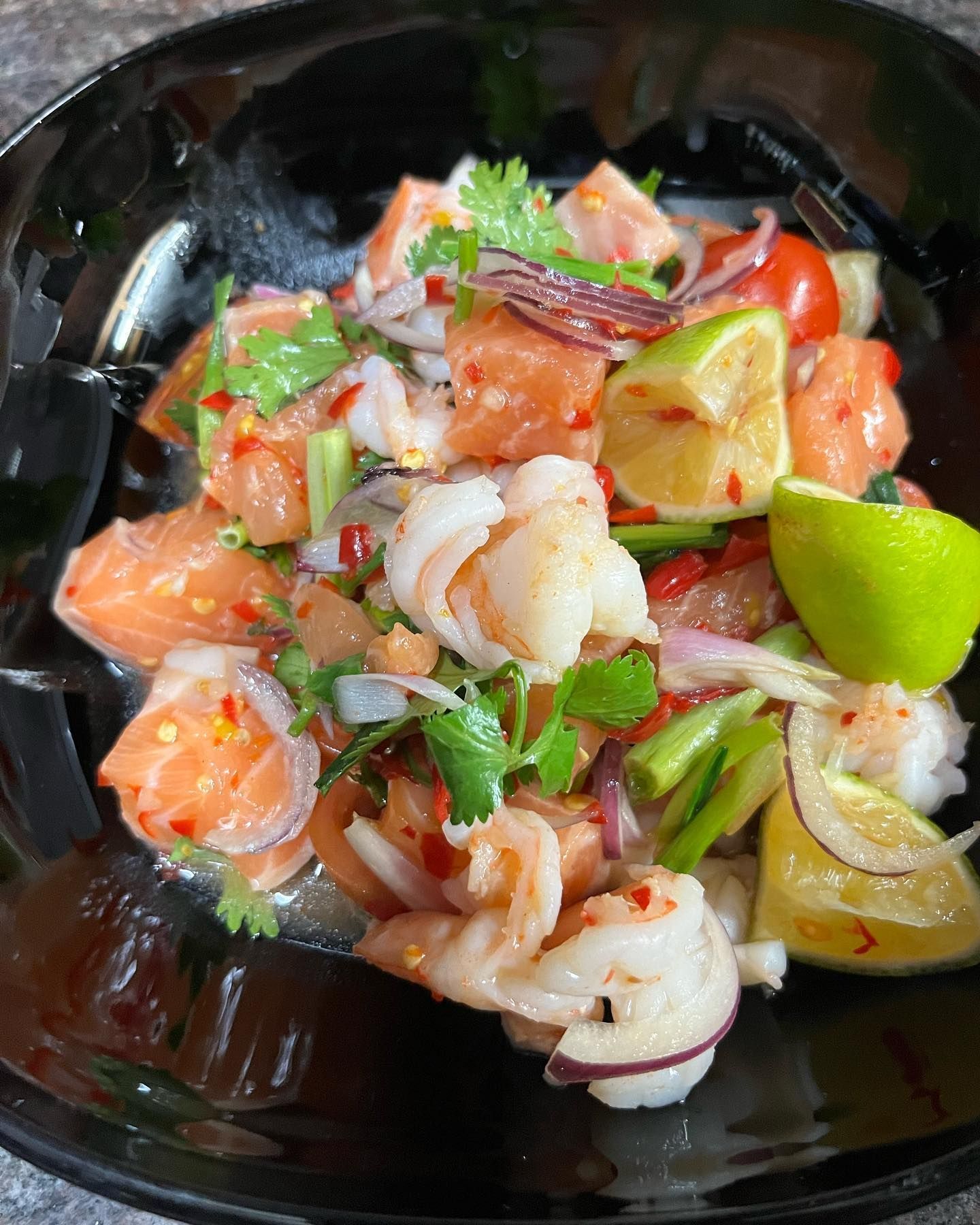 Un bol noir rempli d'une salade de crevettes, de saumon, d'oignons et de citrons verts.