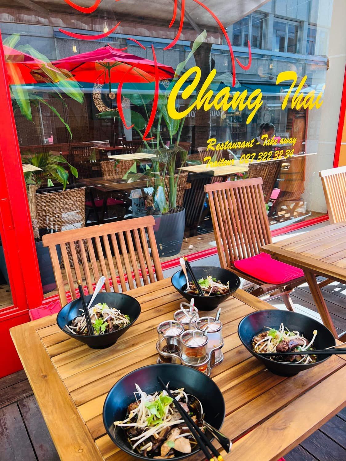 Une table en bois avec des bols de nourriture dessus devant un restaurant.