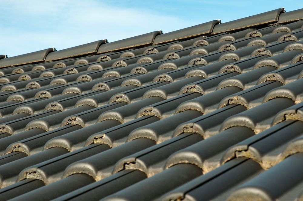 Dark gray ceramic roof tiles against a light blue sky — Geoff Hall Roofing in Port Macquarie, NSW