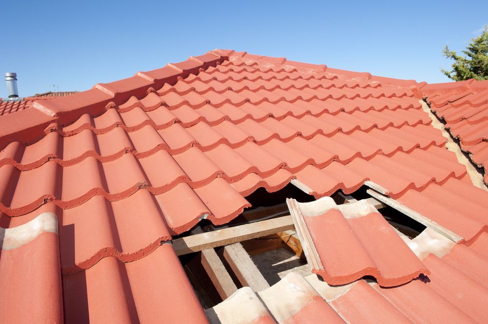 Red tile roof with missing tiles revealing wooden beams and blue sky — Geoff Hall Roofing in Harrington, NSW