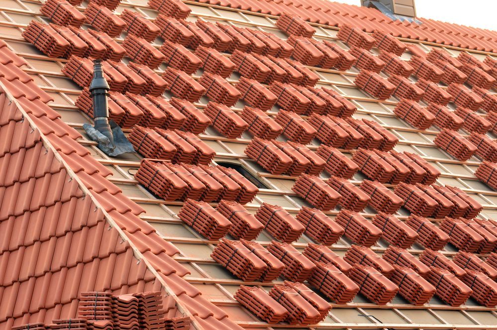 Red roof tiles being installed on a roof, showing bundles and completed sections, daylight — Geoff Hall Roofing in Frederickton, NSW