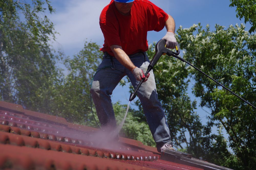 Man power washing a red roof, spraying water in the air under a sunny sky — Geoff Hall Roofing in Port Macquarie, NSW