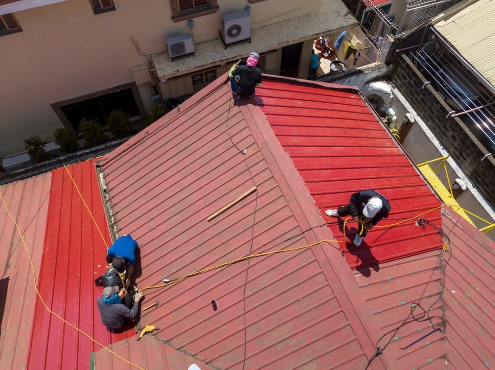 Workers in Safety Gear on A Red Rooftop, Secured by Ropes — Geoff Hall Roofing in Port Macquarie, NSW