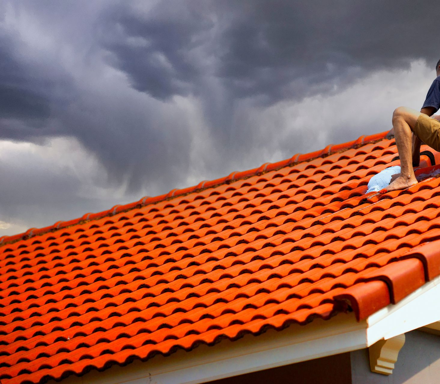 Person on a red tile roof under a cloudy, gray sky, possibly preparing for rain — Geoff Hall Roofing in Port Macquarie, NSW