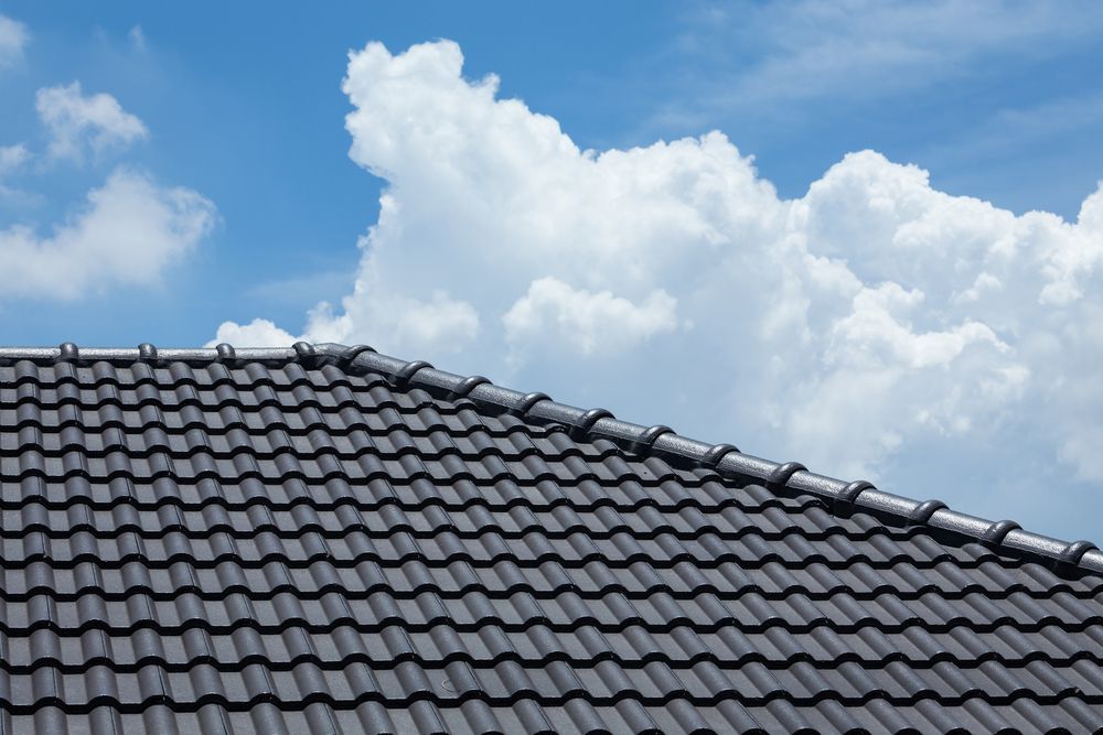 Grey tile roof against a blue sky with puffy white clouds — Geoff Hall Roofing in Wauchope, NSW