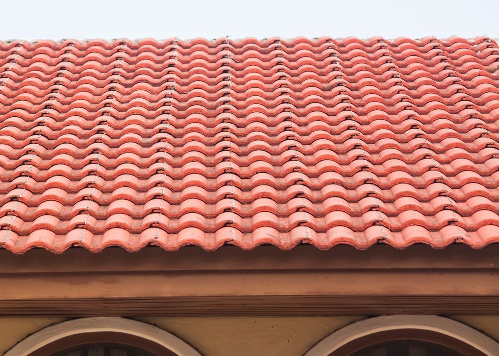 Red clay tile roof on a tan building with arched windows  — Geoff Hall Roofing in Mid North Coast, NSW