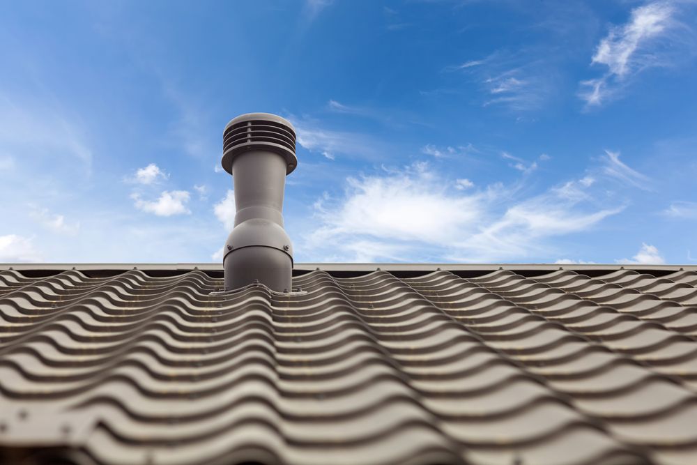 Gray roof with a ventilation pipe against a blue sky with wispy clouds — Geoff Hall Roofing in Wauchope, NSW