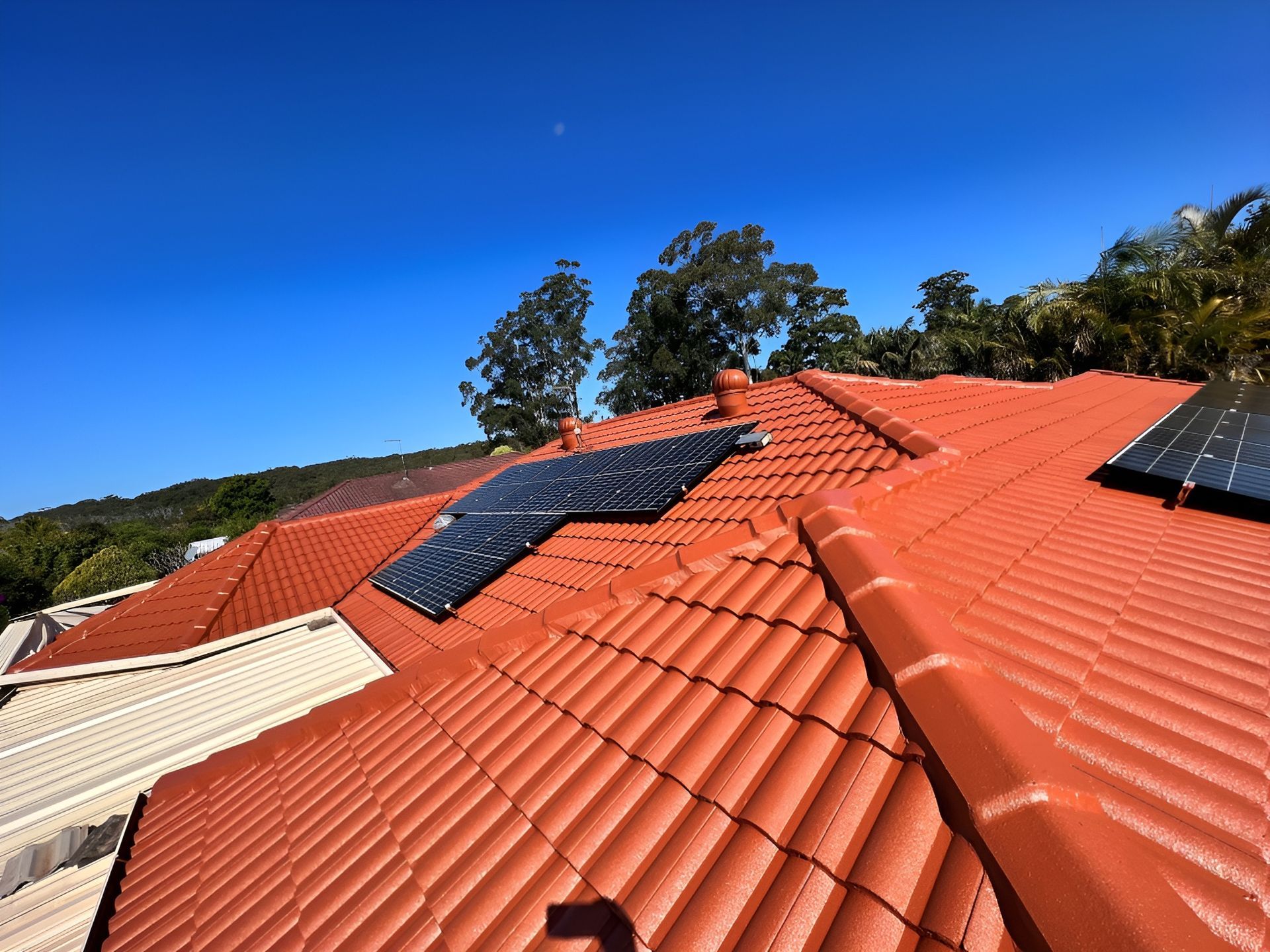 Red-Tiled Roof with Solar Panels Against a Blue Sky — Geoff Hall Roofing in Port Macquarie, NSW