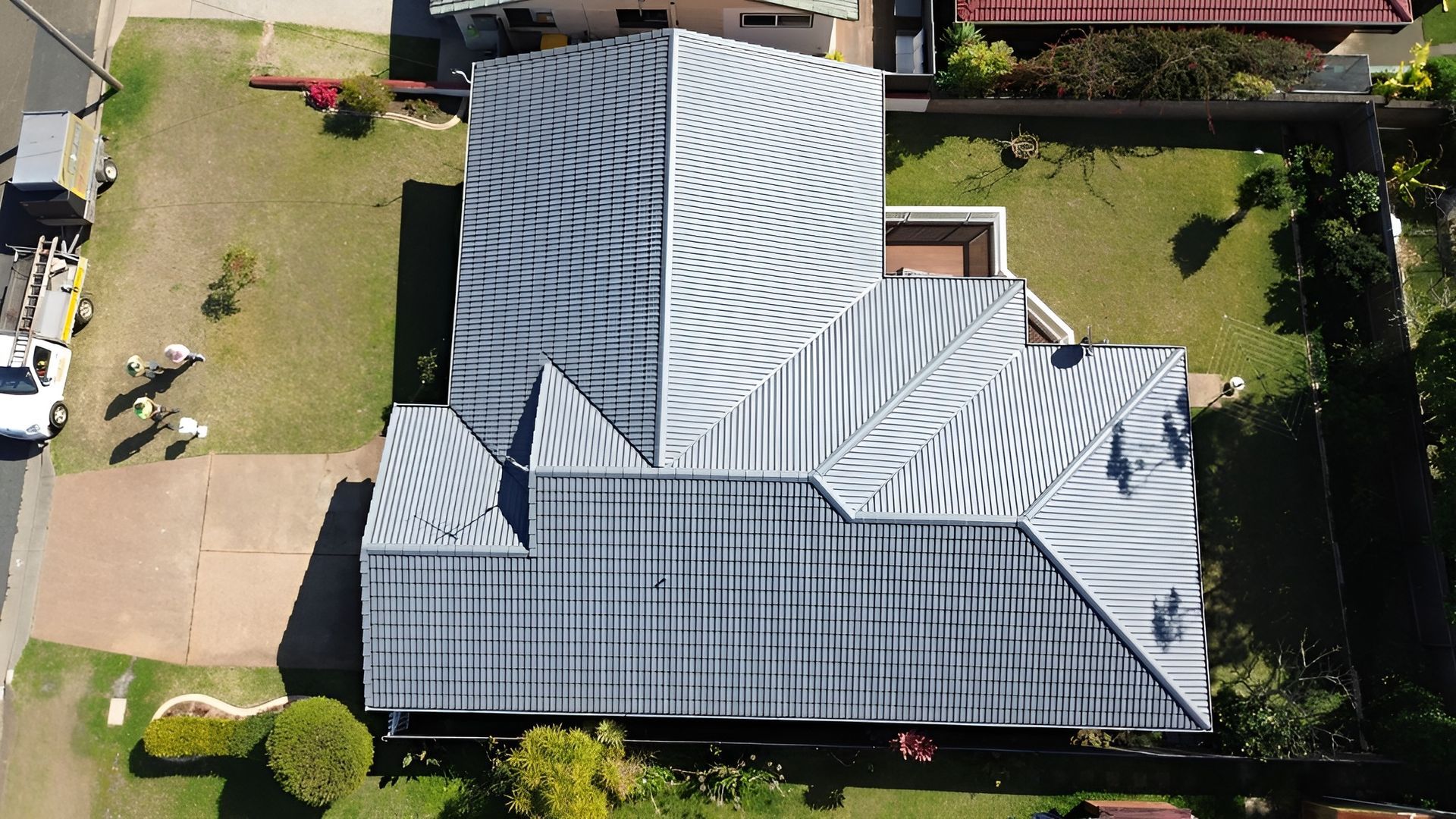 View of A House with A Gray Roof and A Lawn, Street and Surrounding Vegetation — Geoff Hall Roofing in Frederickton, NSW