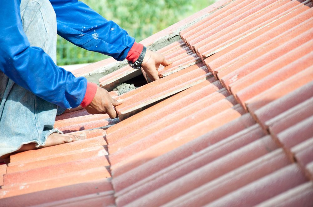 Person installing red clay roof tiles — Geoff Hall Roofing in Wauchope, NSW