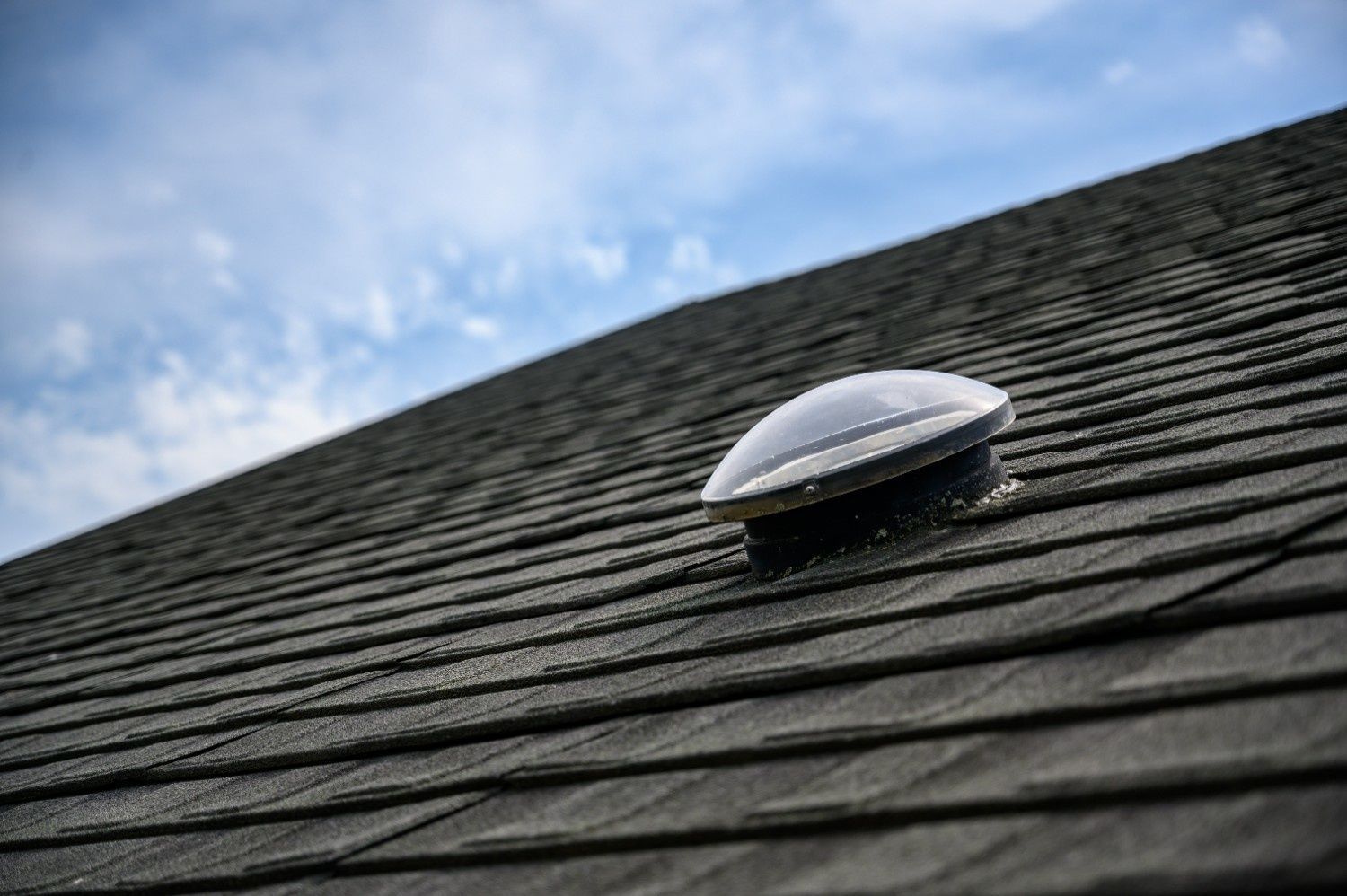 A Dark Asphalt Shingle Roof with A White Dome Vent Against a Blue Sky — Geoff Hall Roofing in Wauchope, NSW