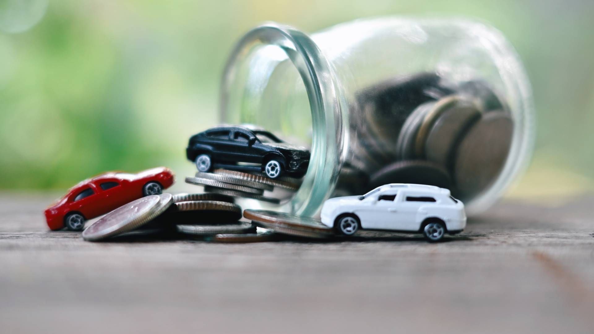 Three toy cars are sitting on top of a pile of coins.