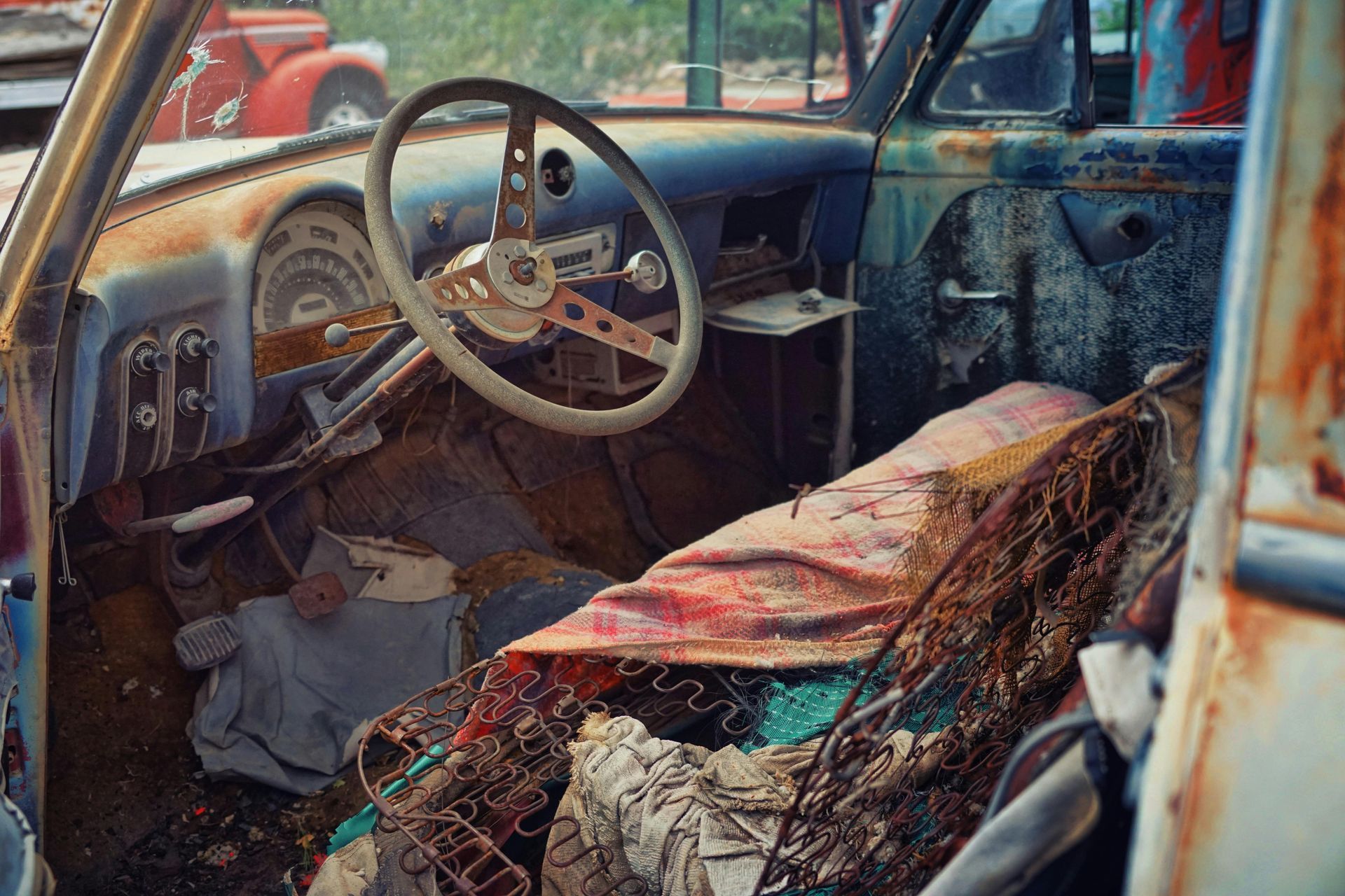 The inside of an old rusty car with a steering wheel and seat.